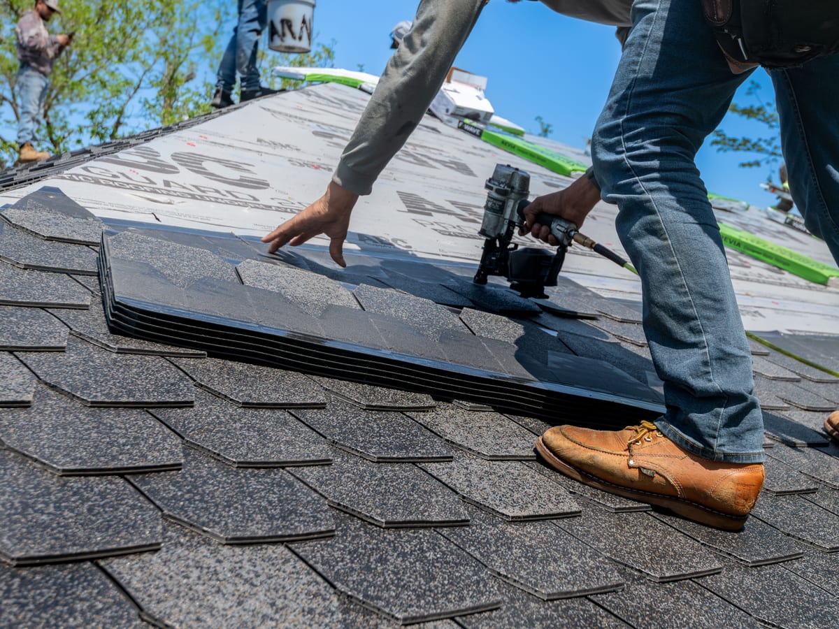 Roofer using nail gun for shingle installation on residential roof.